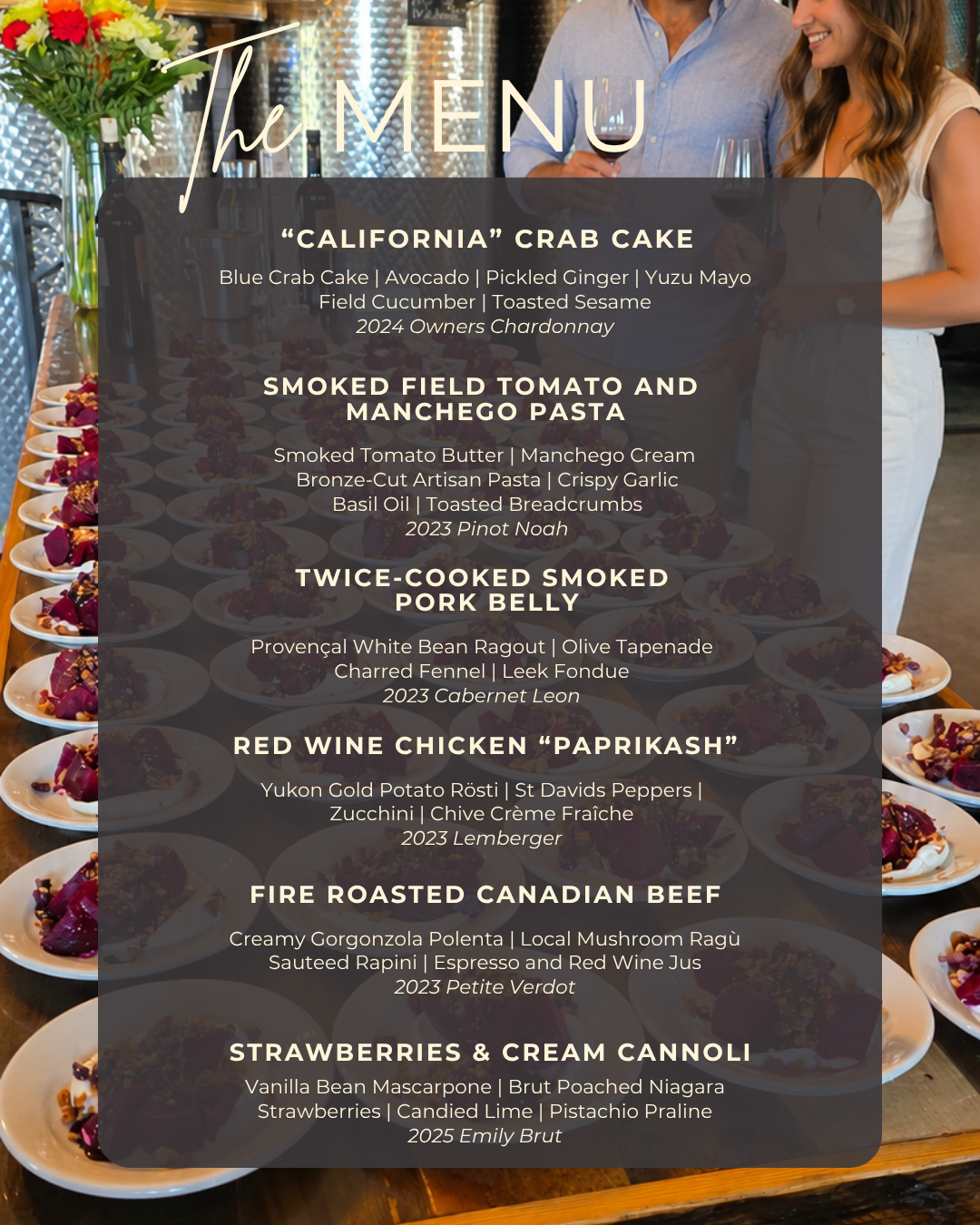 A restaurant menu board displayed in a dining setting, featuring a dark gray menu cover with white text listing crab cake, smoked tomato and manchego pasta, twice-cooked smoked pork belly, red wine chicken paprikash, fire roasted canadian beef, and strawberries and cream cannoli. Plates of food and a smiling couple are visible in the background.